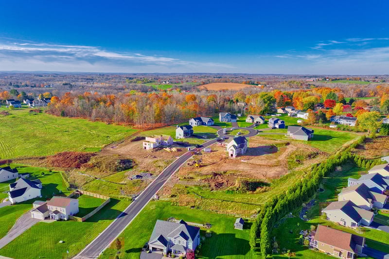 Aerial view of a suburban neighborhood with new home construction, fall foliage, and open land in the Greater Rochester area