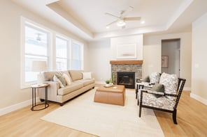 Greater Rochester living room with tan leather ottoman, jute rug, stone fireplace, and large windows