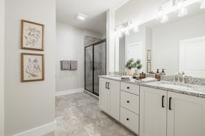 Greater Rochester primary bathroom with double granite vanity, framed shower enclosure, and brushed nickel faucets