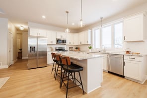 Greater Rochester white shaker kitchen with granite island, black barstools, stainless steel appliances, and glass pendant lights
