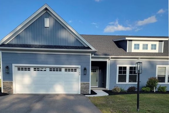 Rochester, NY townhome with blue siding, white trim, an attached two-car garage, paved driveway, and front lawn