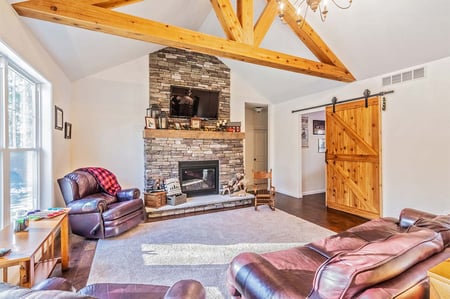 Cozy Greater Rochester area living room with stone fireplace, wood beams, and barn door.