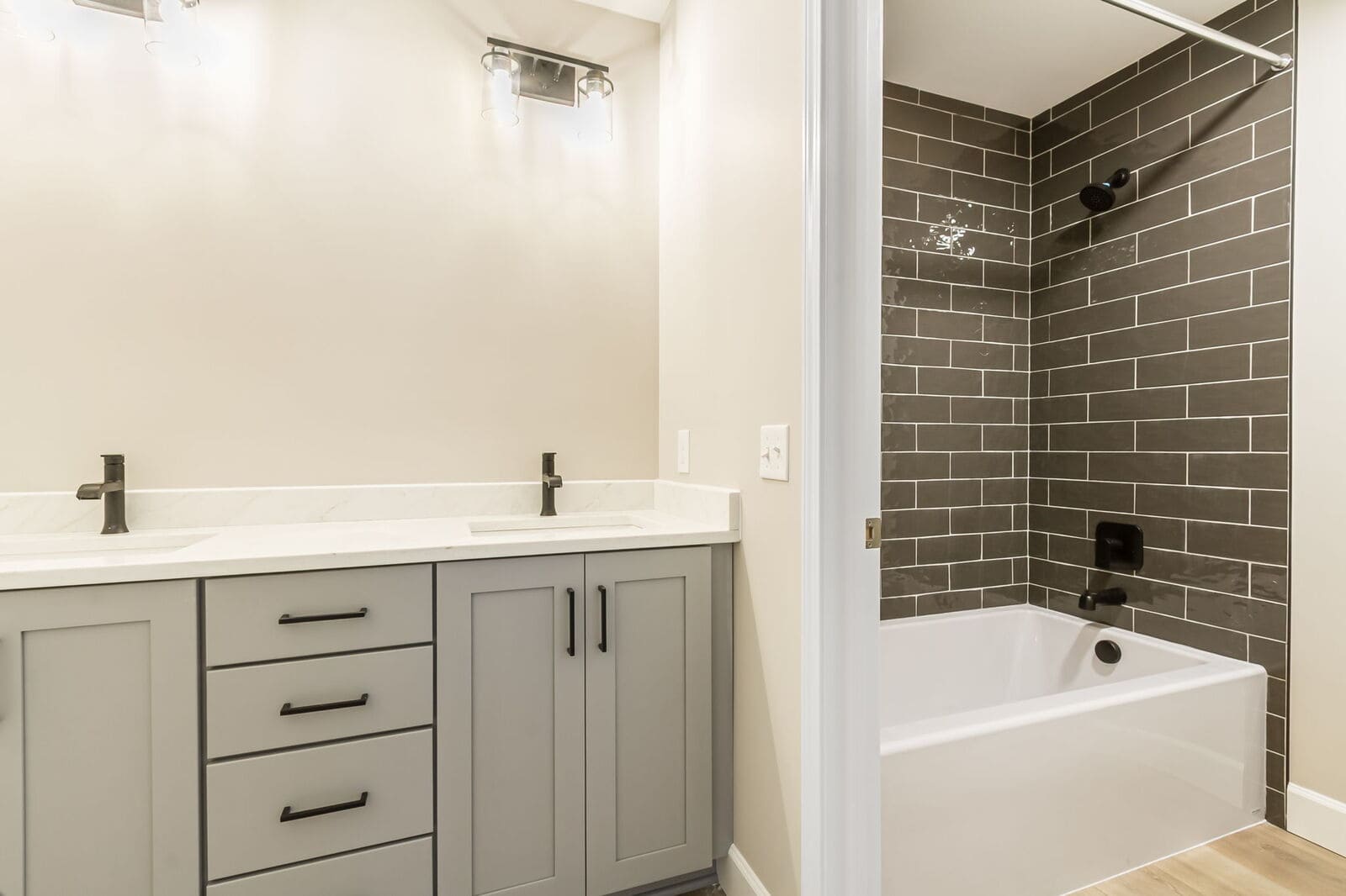 Bathroom with a gray vanity, white countertop, black fixtures, and a tub-shower with dark subway tile.
