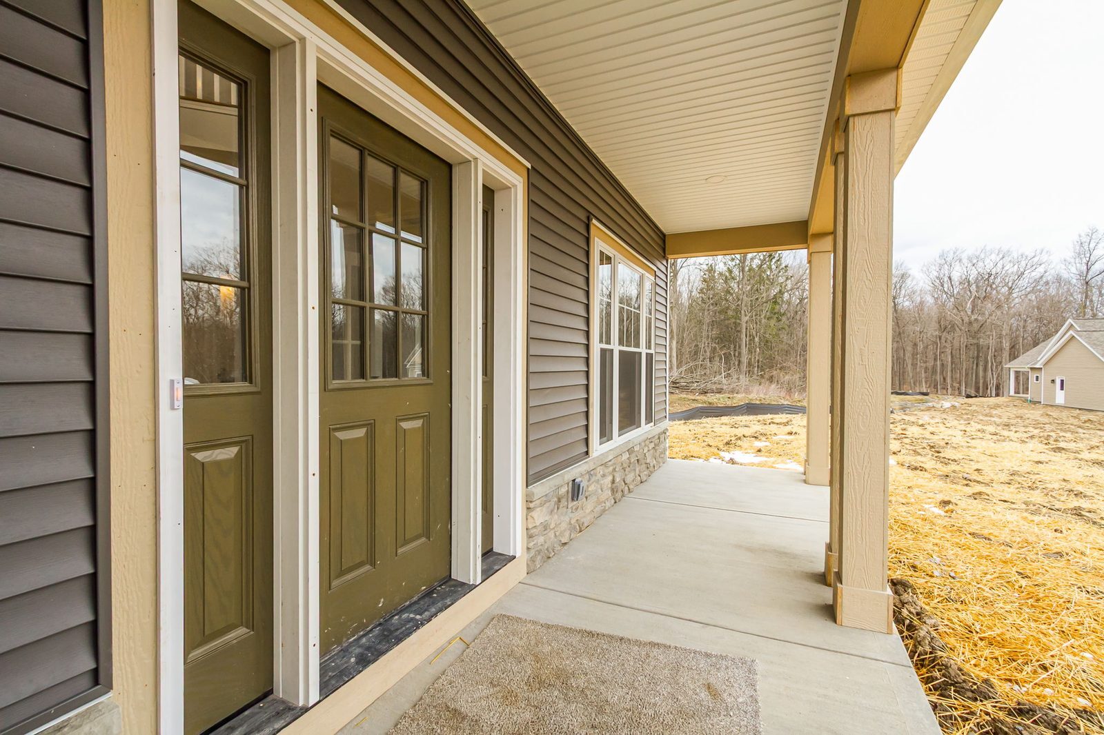 Covered front porch walkway with olive green doors and wooded view