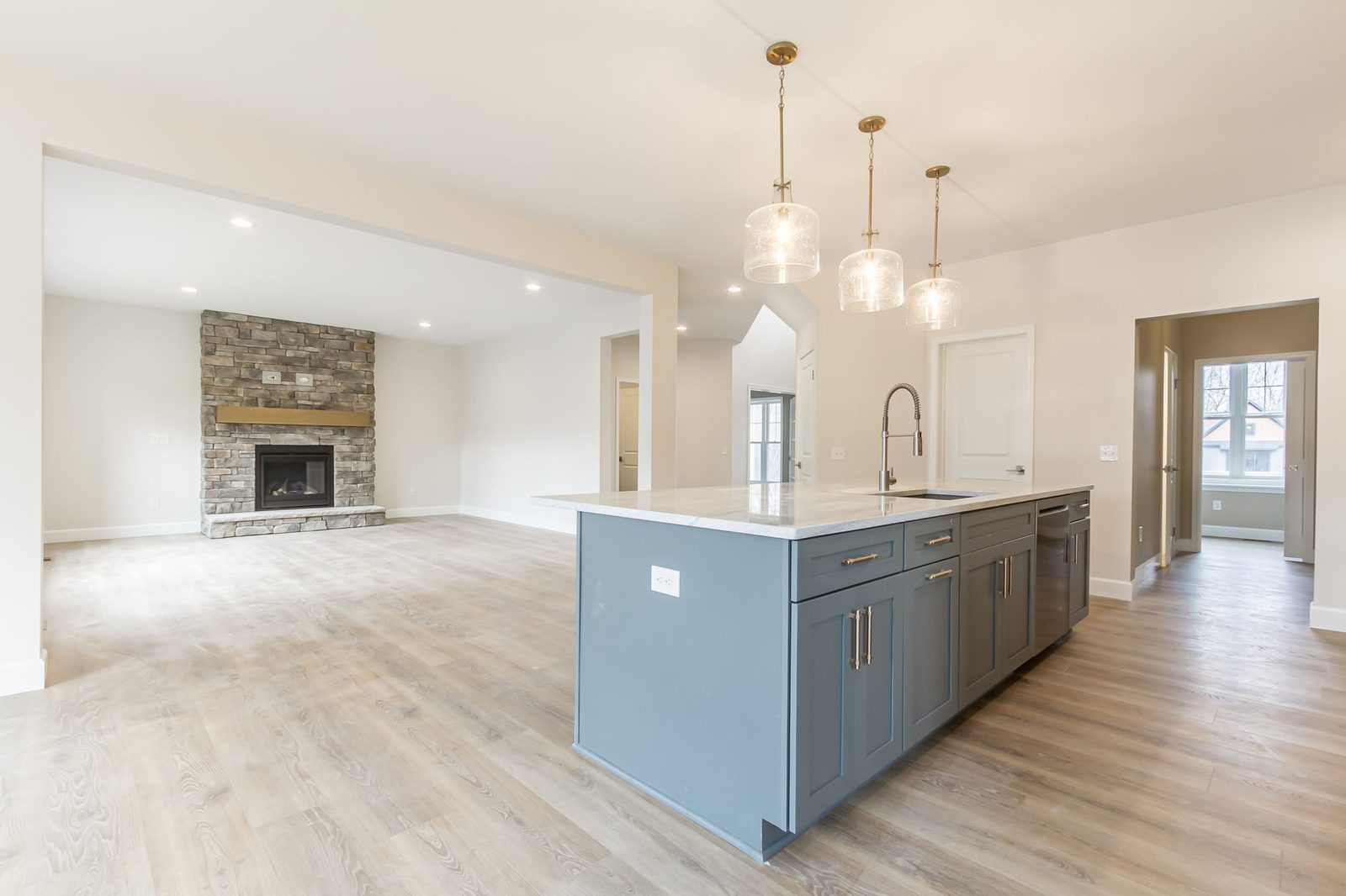 Kitchen island with sink and dishwasher opening to stone fireplace living room