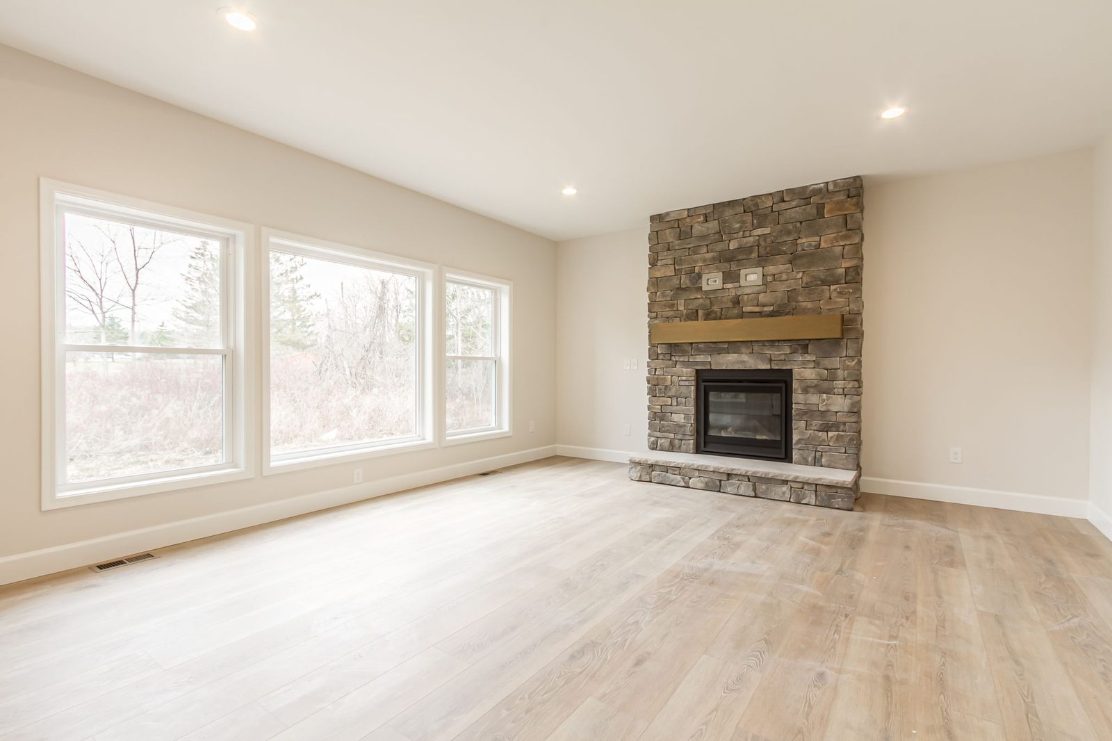 Living room stone fireplace framed by three large windows