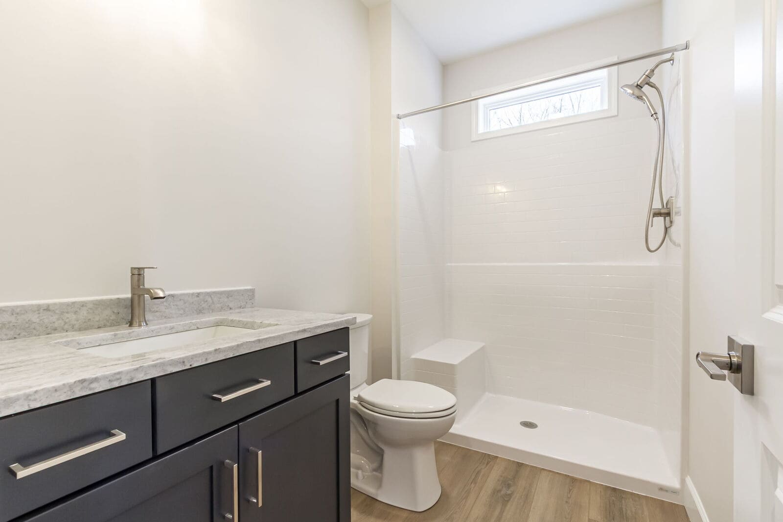 Modern bathroom with dark vanity walk-in shower and light wood flooring in Canandaigua.