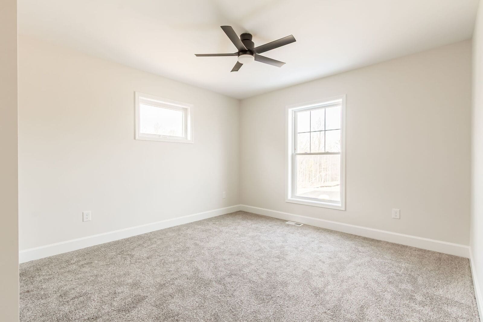 Neutral bedroom with gray carpeting, two windows, and a modern black ceiling fan.
