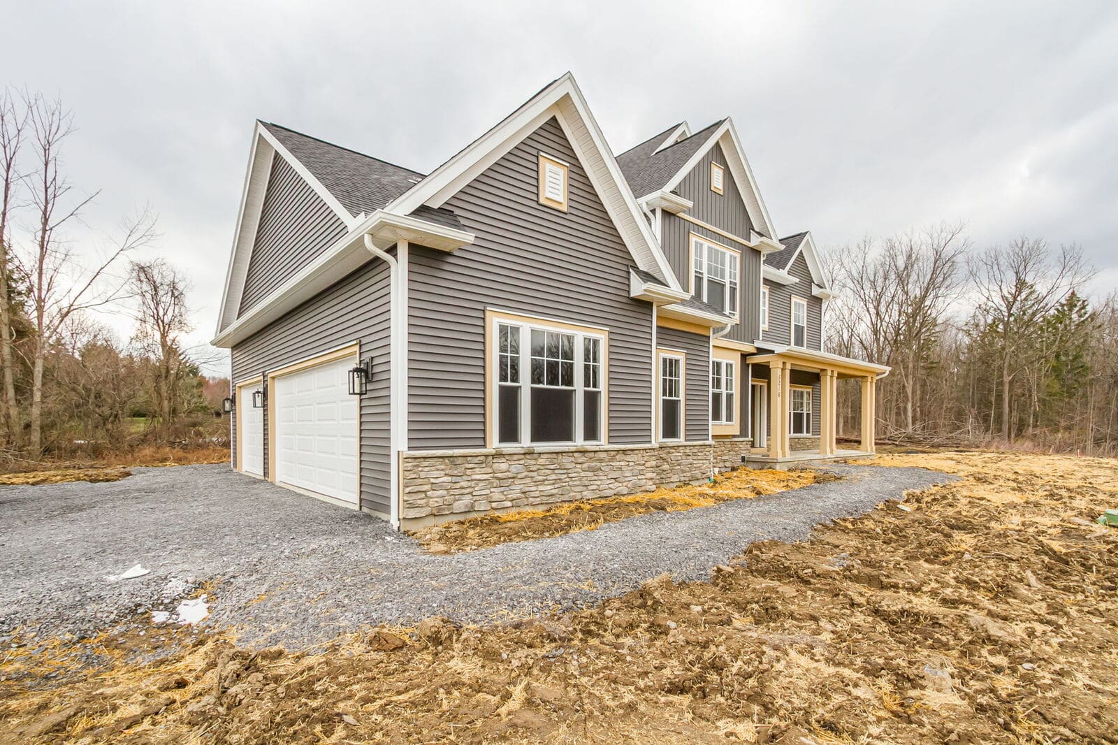 New two-story Canandaigua home with gray siding, stone accents, an attached garage, and a covered front porch.
