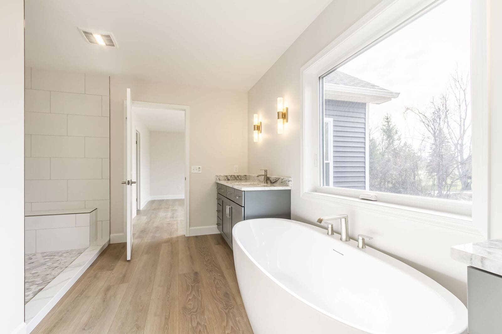 Primary bathroom with a freestanding soaking tub, large window, dark vanity, and walk-in tiled shower.
