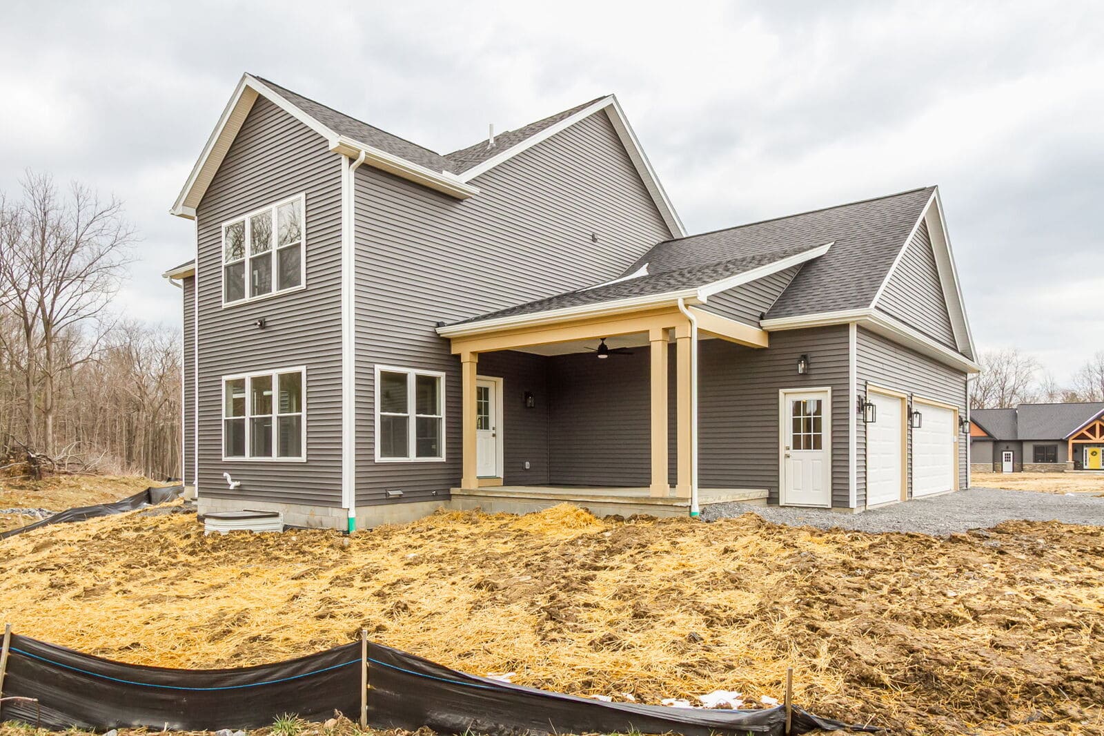 Rear and side view of a new Canandaigua home with gray siding, covered patio, and attached garage.