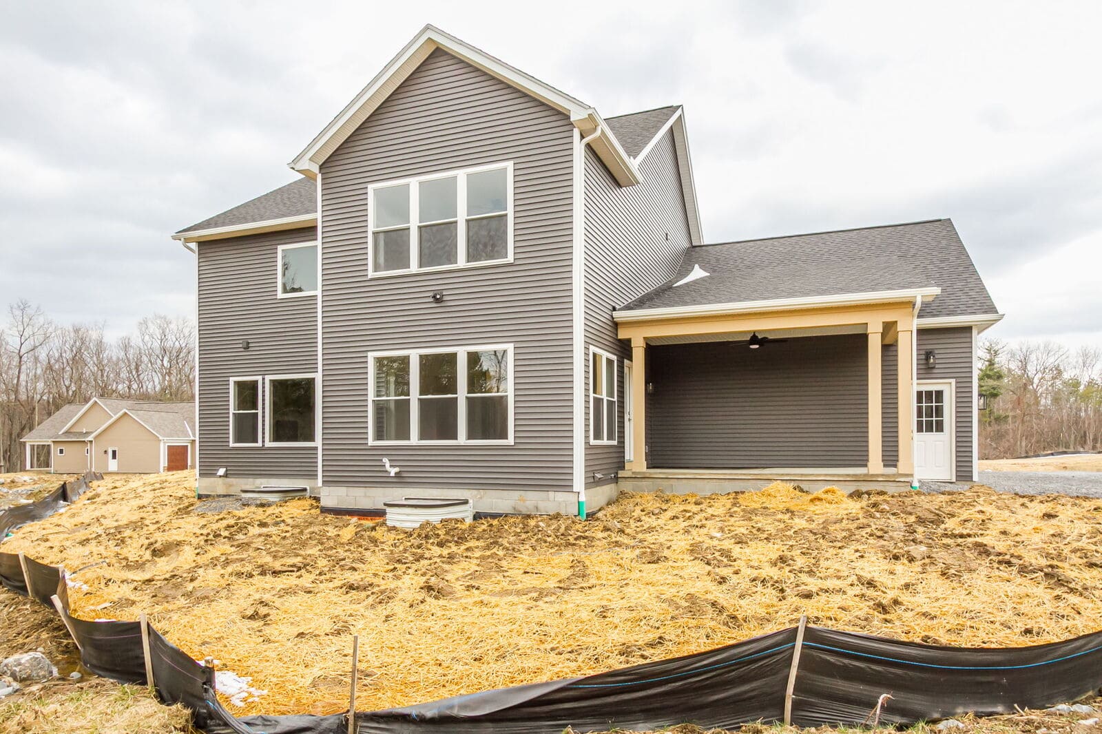 Rear view of a new two-story Canandaigua home with gray siding, large windows, and a covered patio.