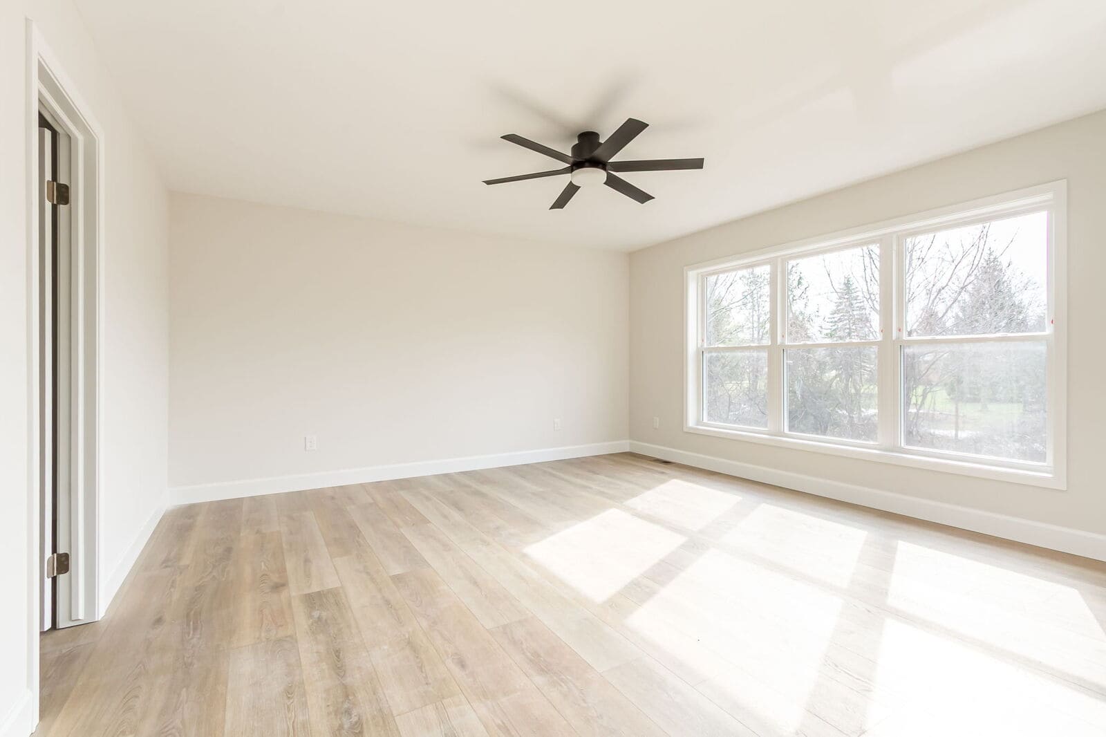 Spacious primary bedroom with light wood flooring, large windows, and a black ceiling fan.