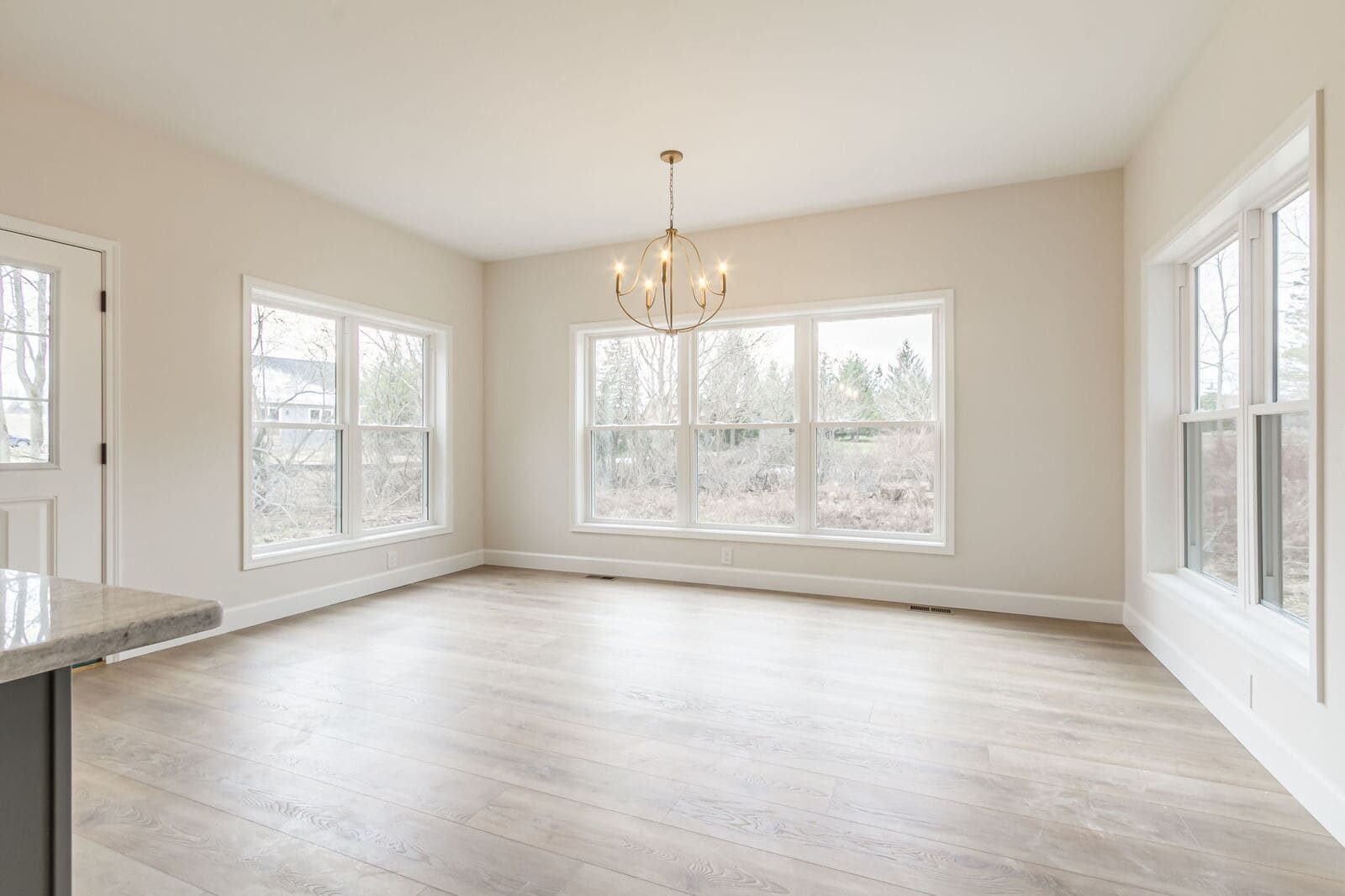 Sunlit dining area with wide plank flooring and large windows in a new Canandaigua home.