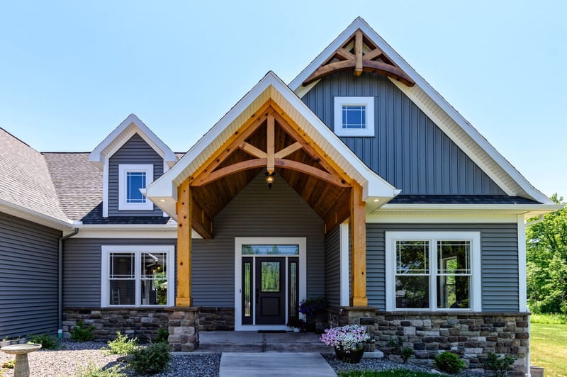 Gabled exterior wood brackets on custom home entryway on sunny day with stone veneer siding