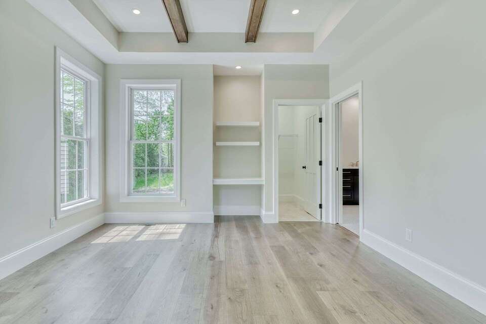 Master Suite With Build-in Shelving, On-Suite Full Bathroom, Tray Ceiling With Wooden Beams, Recessed Lighting, Wooden Flooring, and Tall Windows