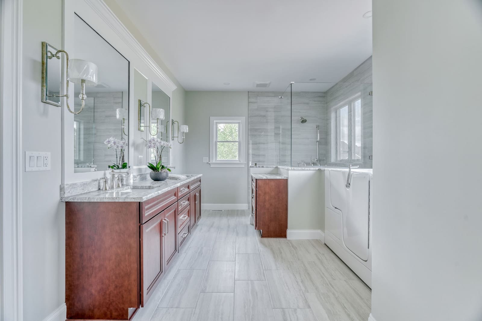 Accessible primary bathroom with warm wood vanity, glass shower, walk-in tub, and soft neutral finishes.