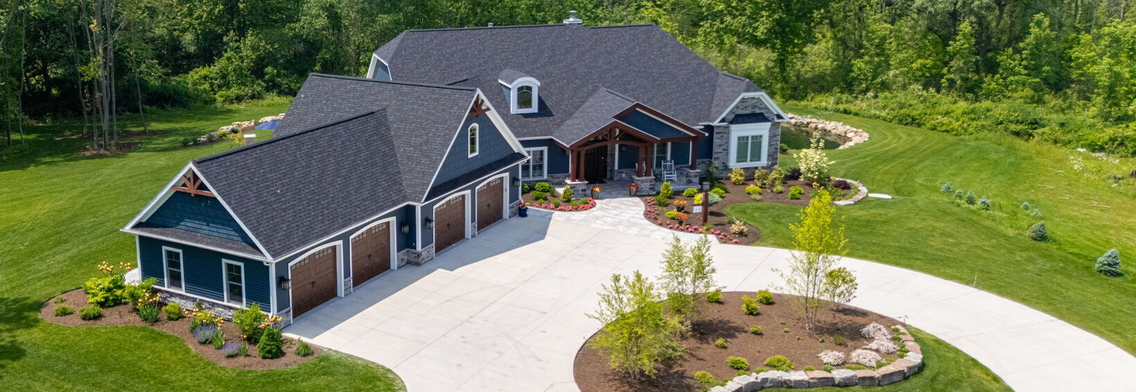 Aerial view of blue custom home with circular driveway, landscaped front yard, and pond in the distance_1
