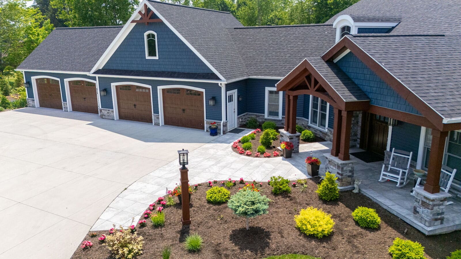 Aerial view of blue custom home with wood garage doors, landscaped entry, and wide concrete driveway.