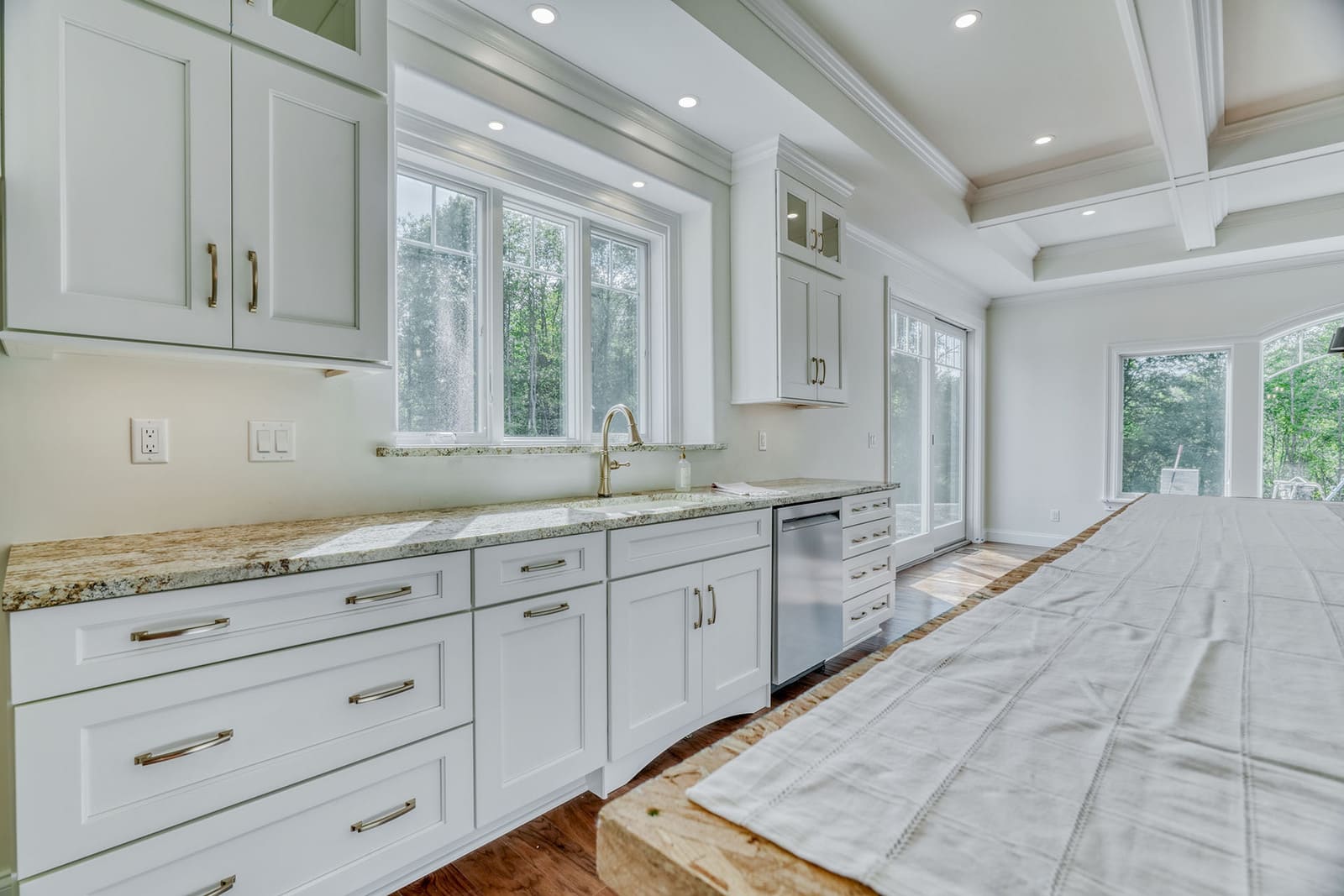 Bright custom kitchen with white cabinetry, oversized island, granite countertops, and wooded views.