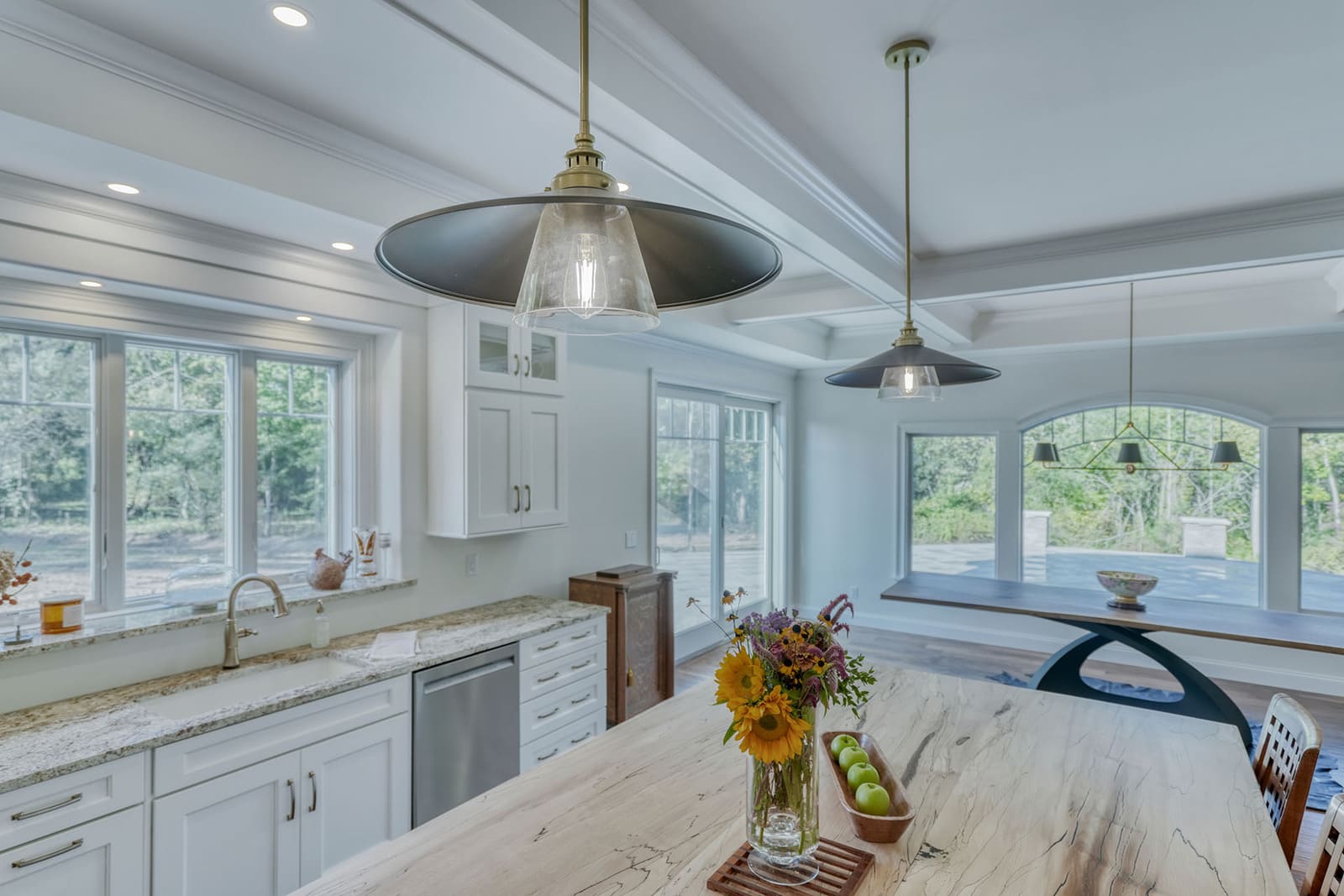 Bright kitchen and dining area with pendant lights, large island, white cabinets, and wooded views.