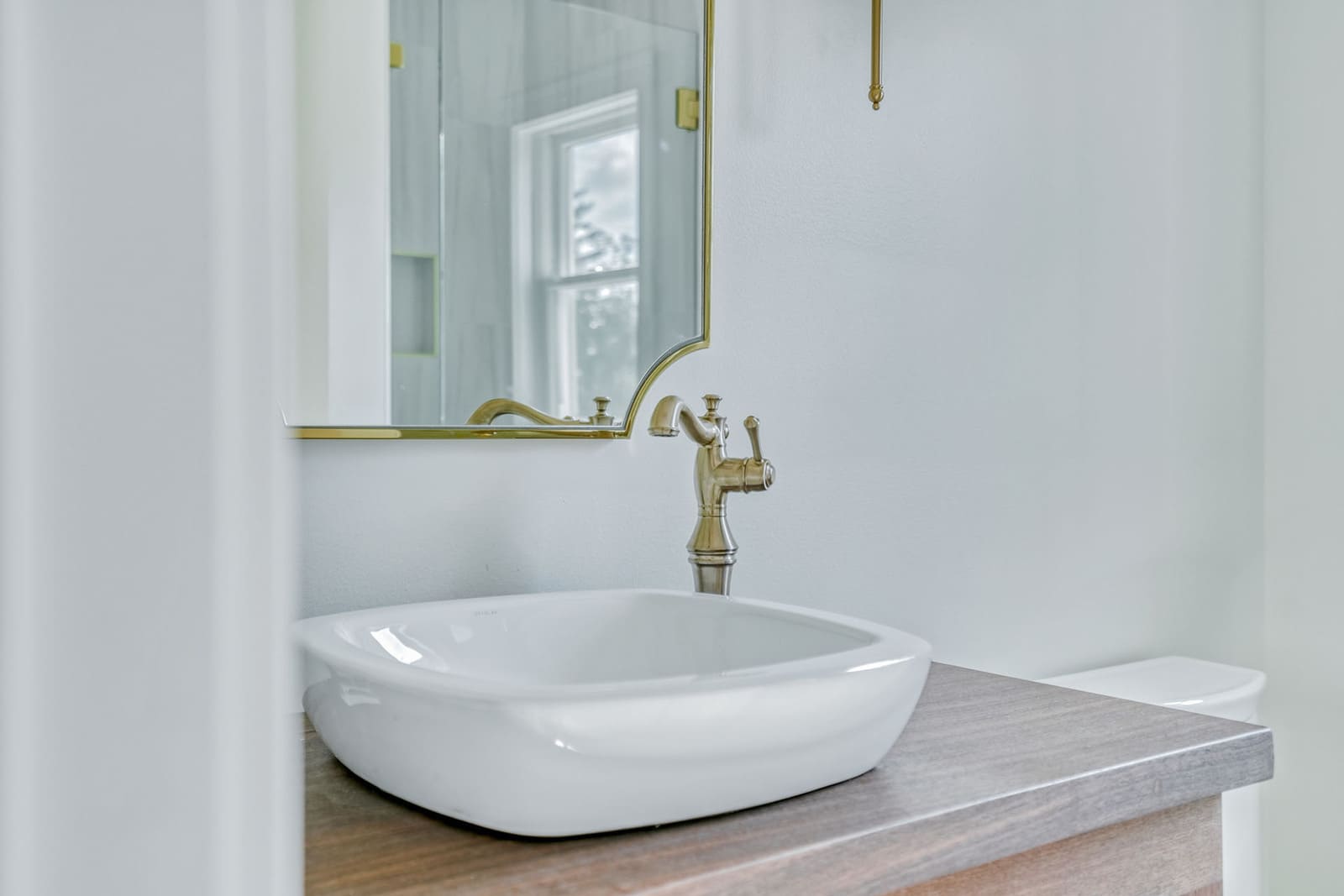 Close-up of bathroom vessel sink with brass faucet, wood vanity, and gold-framed mirror.