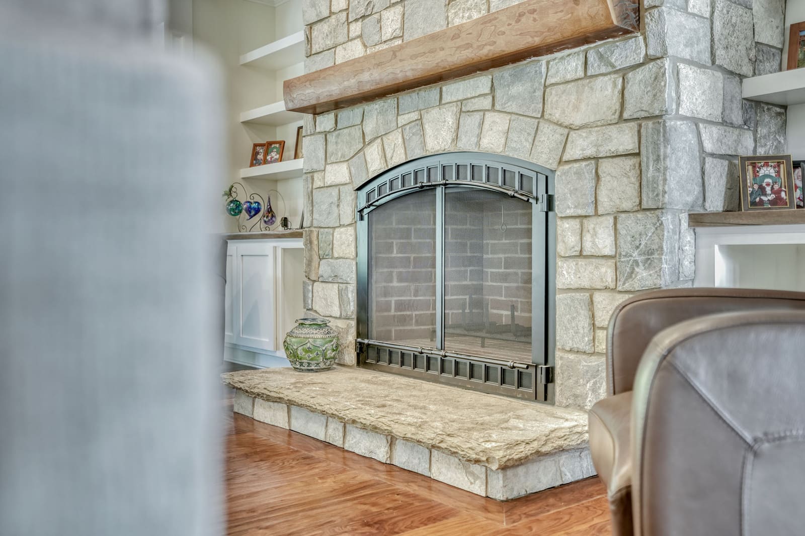 Close-up of stone fireplace with wood mantel, built-in shelves, and hardwood floors in custom home.