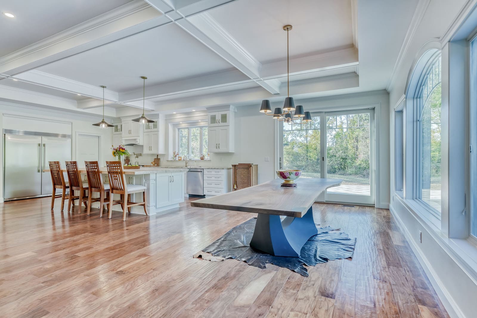 Open kitchen and dining area with coffered ceiling, large windows, hardwood floors, and island seating.