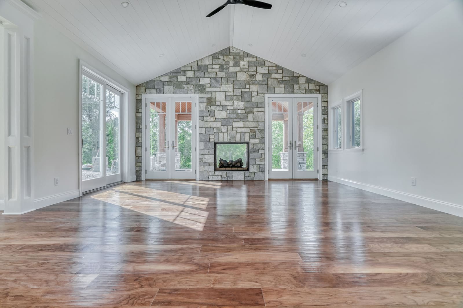 Sunroom with vaulted shiplap ceiling, stone fireplace wall, hardwood flooring, and French doors to outdoor living spaces.