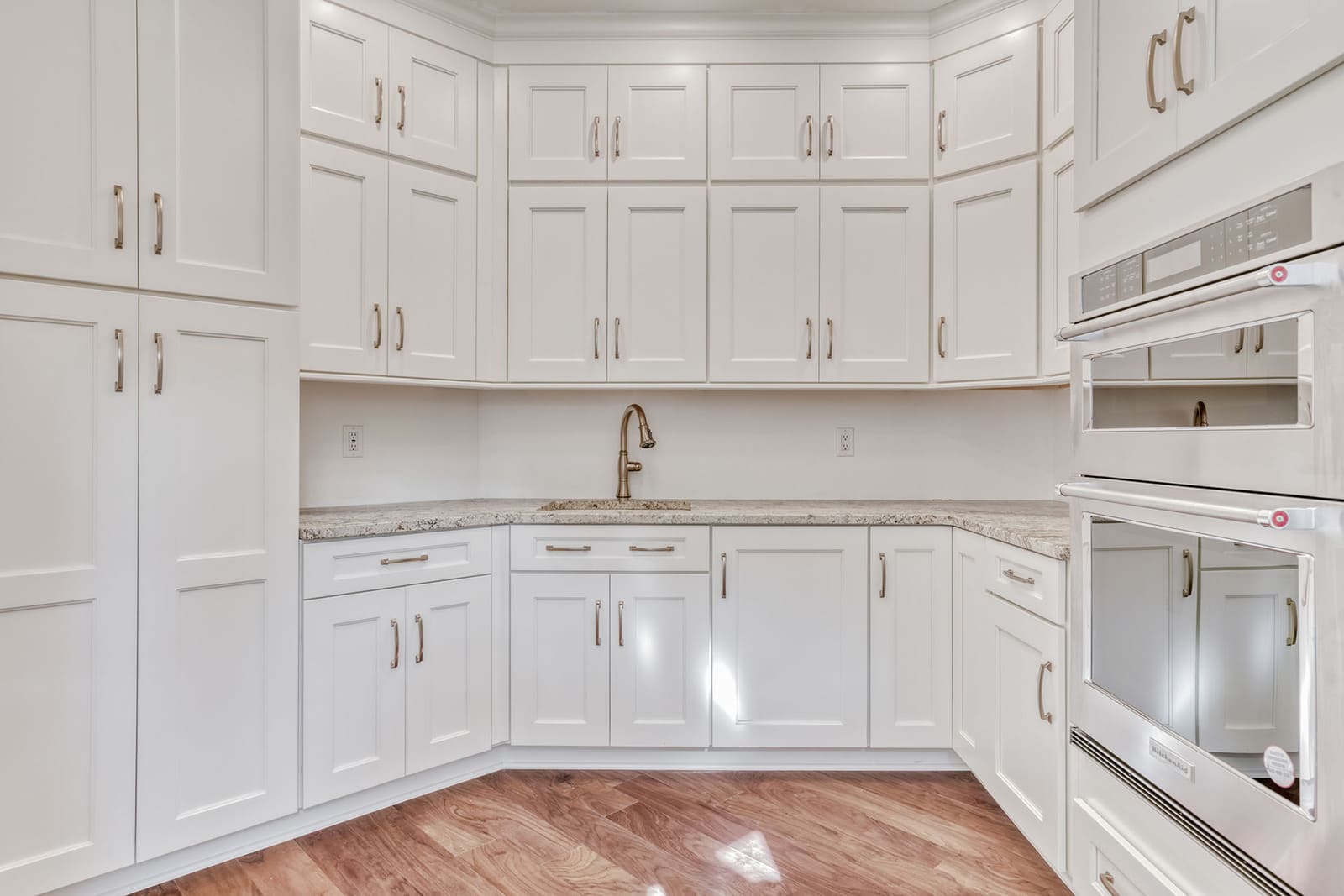 White butler’s pantry with tall cabinets, granite counters, wall oven, sink, and hardwood floors.
