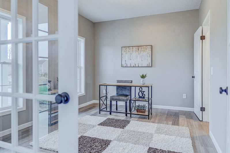 Bright home office with glass doors, modern desk, area rug, and neutral wall tones by Gerber Homes