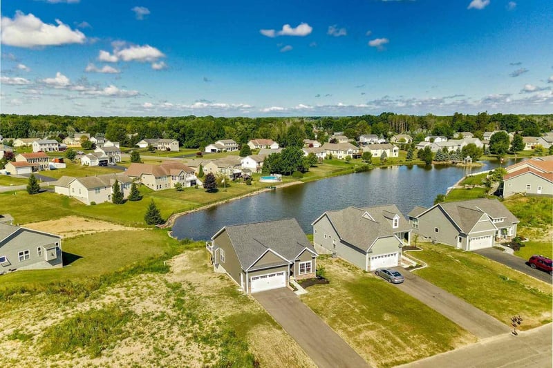 Aerial view of homes surrounding a pond in a suburban neighborhood in the Greater Rochester area under a blue sky