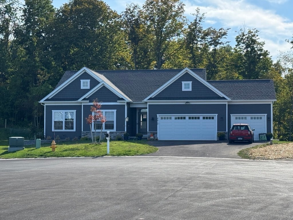 Single-story home with 3-car garage in Rochester, NY, backed by tall trees and blue sky