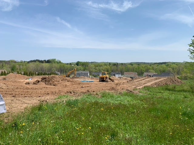 Excavator clearing land for new construction home on sunny day