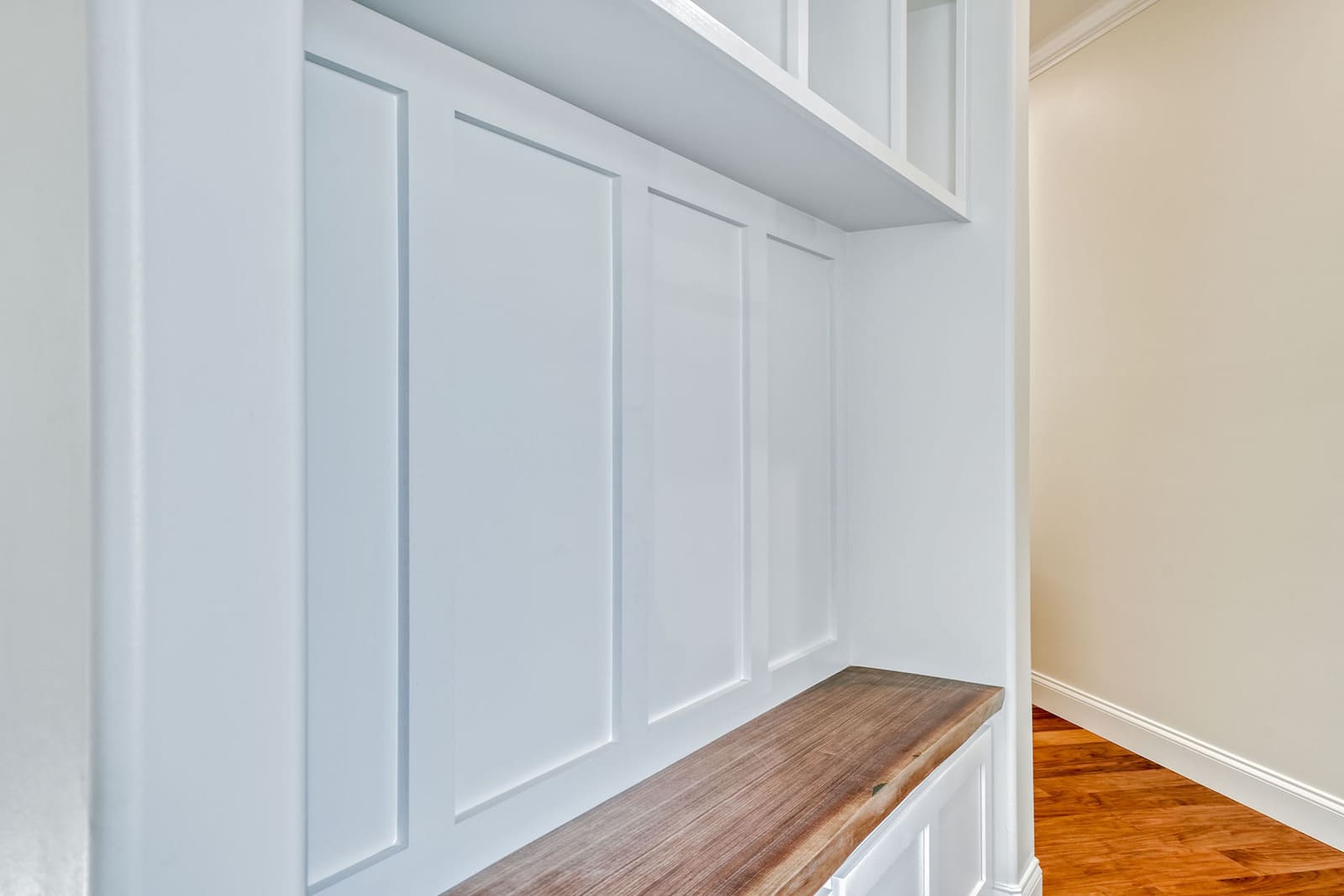 Custom mudroom bench with white paneled built-ins, wood seat, upper storage, and hardwood flooring.