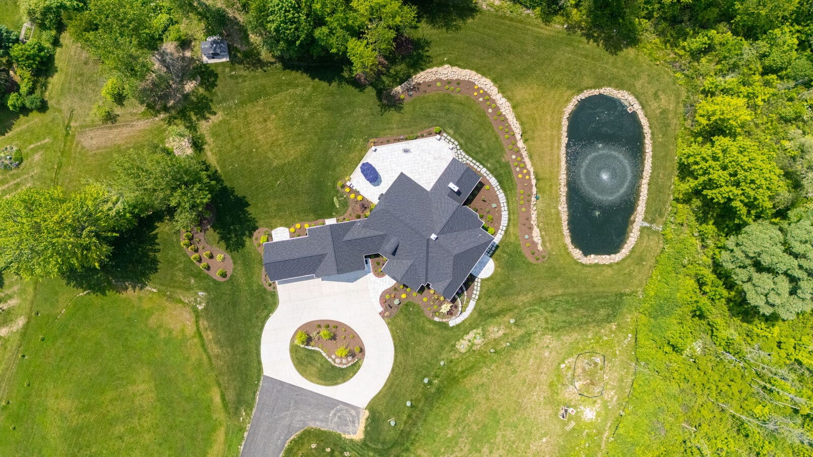 Overhead view of custom home property with pond, patio, circular driveway, and expansive lawn