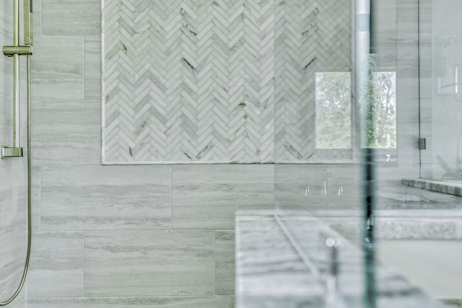 Primary shower detail with marble-look herringbone accent tile, glass enclosure, and soft gray wall tile