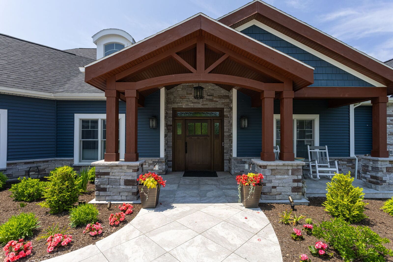 Timber-framed front entry with stone columns, flower planters, blue siding, and custom wood door